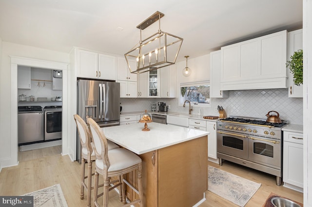 kitchen with washer and clothes dryer, appliances with stainless steel finishes, light wood-style floors, white cabinetry, and a sink