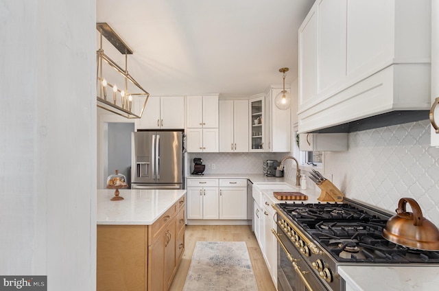 kitchen with pendant lighting, a sink, backsplash, stainless steel appliances, and glass insert cabinets