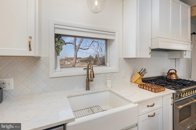 kitchen featuring a sink, backsplash, stainless steel stove, white cabinets, and light stone countertops