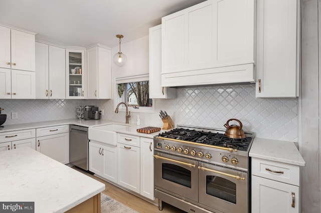 kitchen with glass insert cabinets, light stone countertops, white cabinets, stainless steel appliances, and a sink