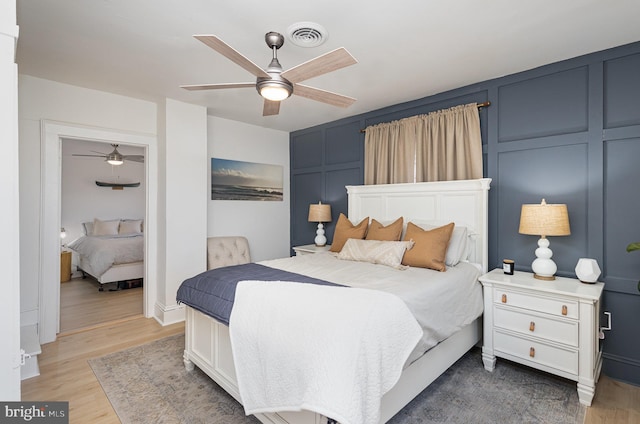 bedroom with visible vents, wood finished floors, a ceiling fan, and a decorative wall