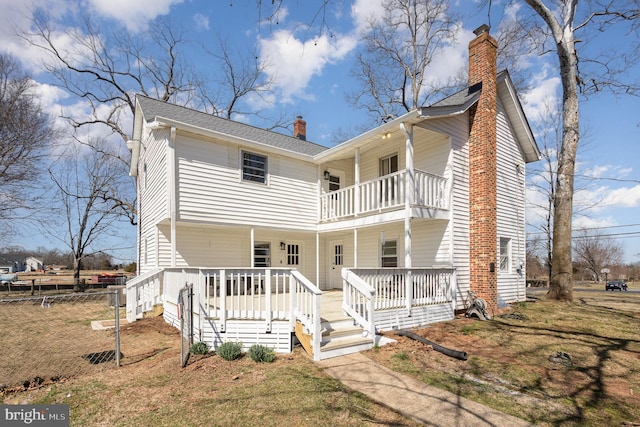 back of property with a chimney, a balcony, and fence