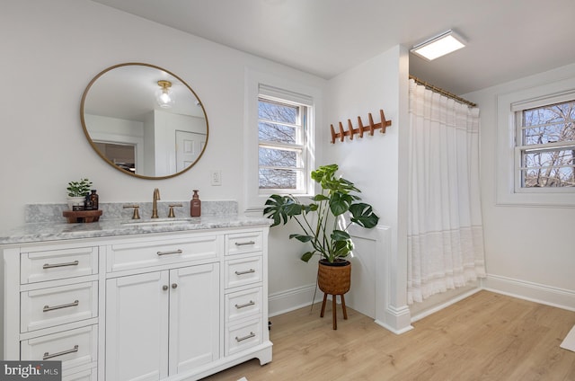 full bath featuring vanity, wood finished floors, a healthy amount of sunlight, and baseboards