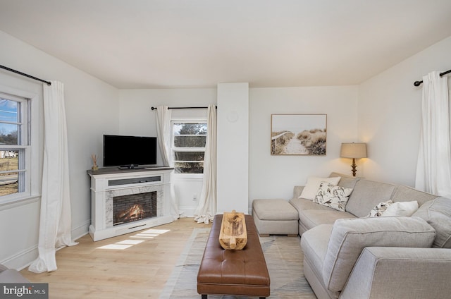 living room featuring light wood-style flooring, baseboards, and a lit fireplace