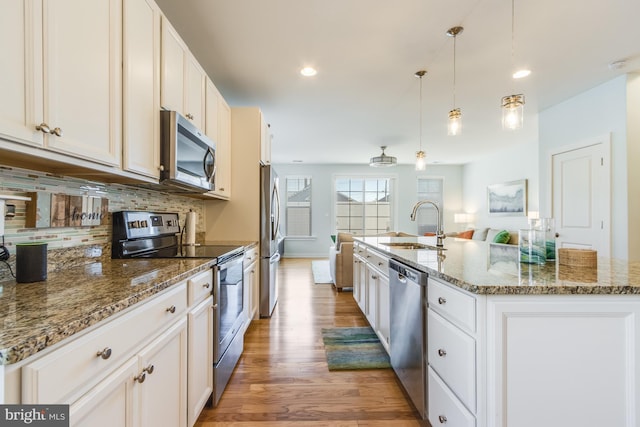 kitchen with stainless steel appliances, decorative backsplash, a kitchen island with sink, a sink, and light wood-type flooring