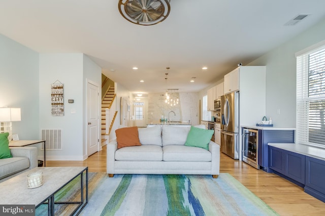 living room with beverage cooler, visible vents, light wood finished floors, and stairs