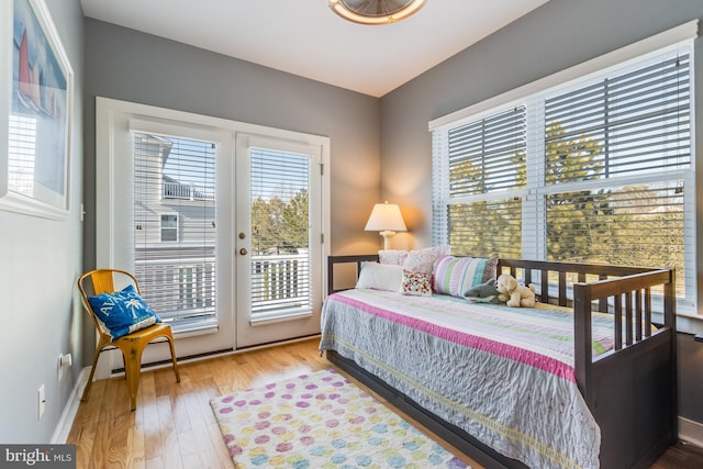 bedroom featuring access to exterior, multiple windows, baseboards, and wood finished floors