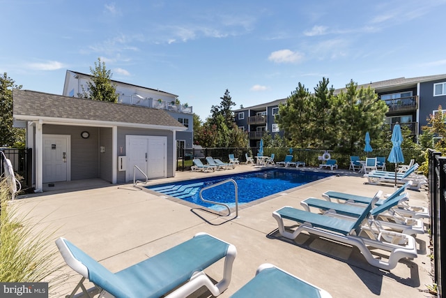 community pool featuring a patio area, fence, and an outbuilding