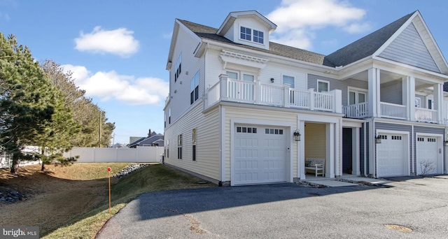 view of front of property with driveway, an attached garage, fence, and a balcony