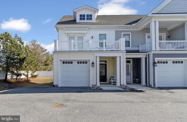 view of front facade featuring a balcony, an attached garage, aphalt driveway, and roof with shingles