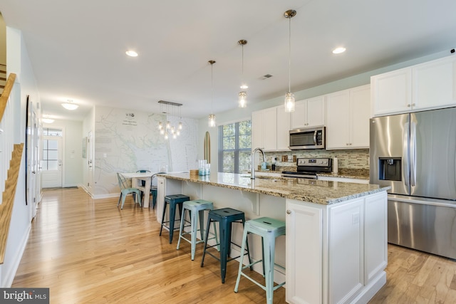 kitchen featuring tasteful backsplash, stainless steel appliances, light wood-type flooring, white cabinetry, and a sink