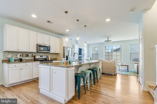 kitchen with a center island with sink, decorative backsplash, stainless steel appliances, light wood-type flooring, and white cabinetry