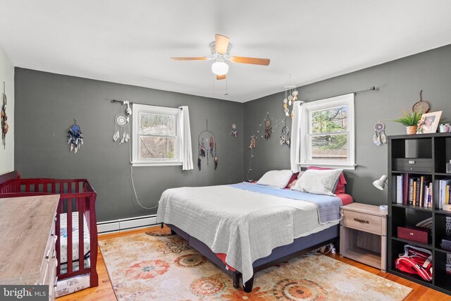 bedroom featuring a baseboard heating unit, wood finished floors, and a ceiling fan