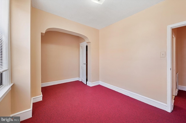 carpeted empty room featuring arched walkways and baseboards