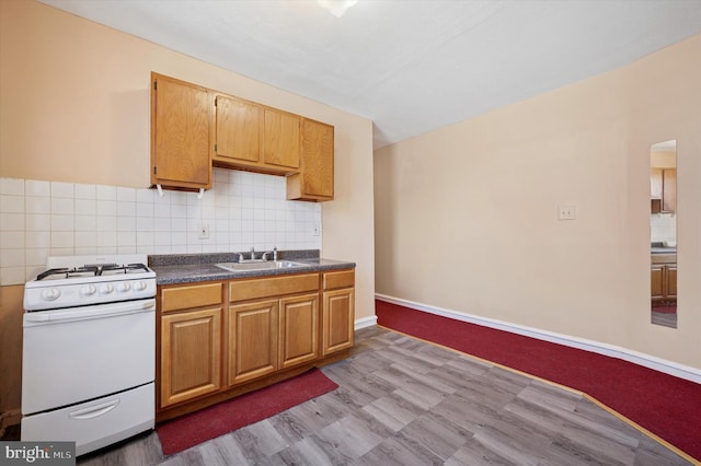 kitchen featuring dark countertops, white gas range, backsplash, and a sink