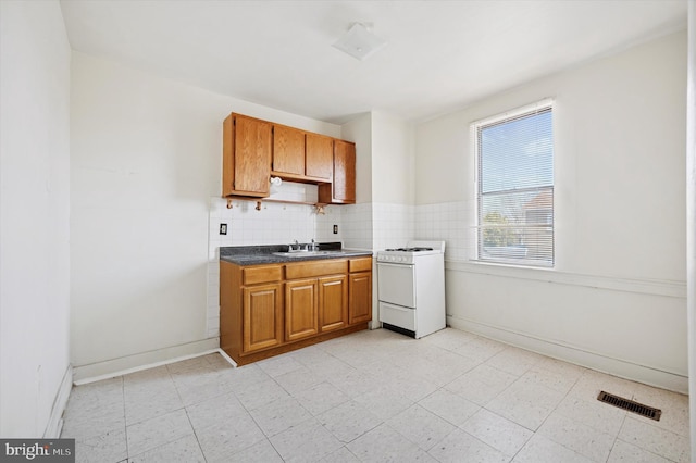 kitchen with brown cabinetry, visible vents, white gas range, a sink, and tasteful backsplash