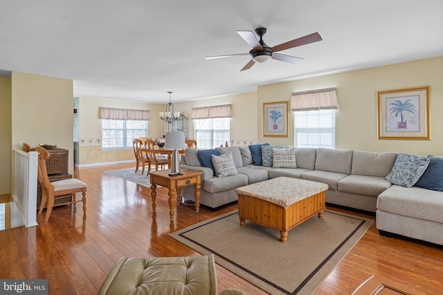 living area with baseboards, hardwood / wood-style floors, and ceiling fan with notable chandelier