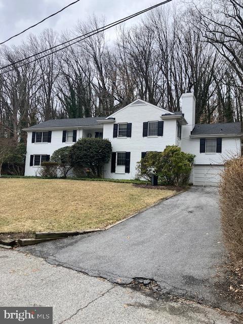 view of front facade featuring driveway, a chimney, and a front yard