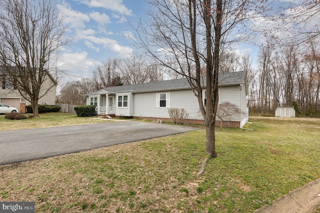 single story home featuring an outdoor structure, a storage unit, a front lawn, and a shingled roof