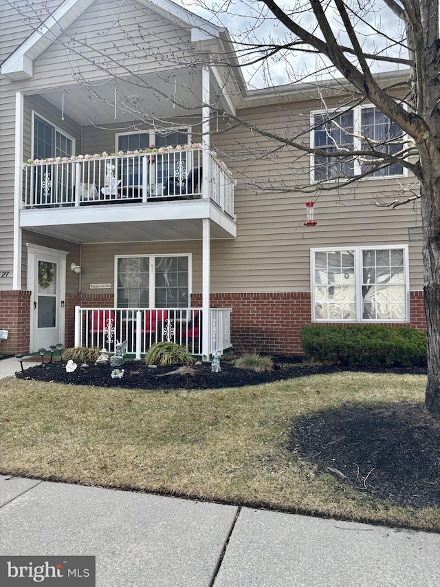 view of property exterior featuring covered porch, brick siding, a lawn, and a balcony