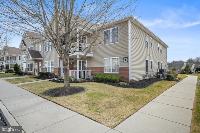 view of front of house with a balcony, a front yard, a residential view, and brick siding