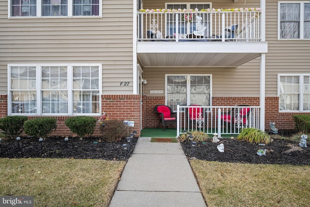 view of exterior entry featuring covered porch, brick siding, and a balcony