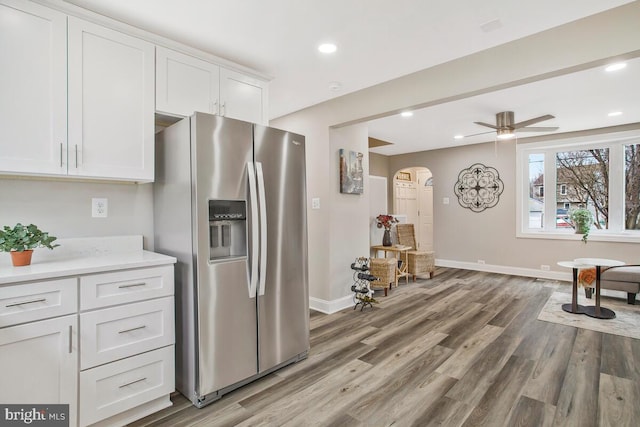 kitchen featuring arched walkways, stainless steel fridge with ice dispenser, light wood-style flooring, light countertops, and white cabinetry