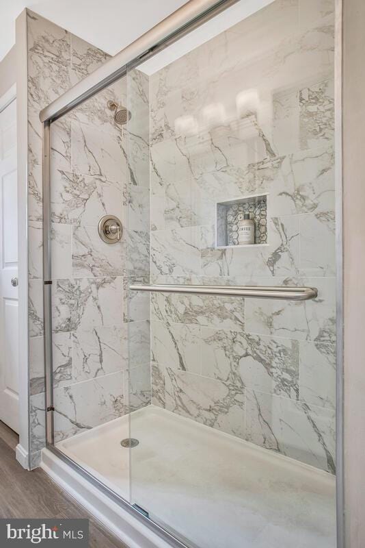 bathroom with a marble finish shower and wood finished floors