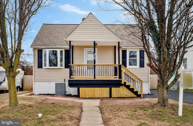 bungalow-style home featuring a porch, central air condition unit, a shingled roof, fence, and a chimney