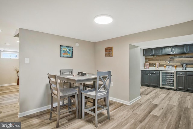 dining room with light wood-type flooring, beverage cooler, indoor bar, and baseboards