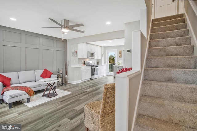 living area with ceiling fan, stairway, light wood-type flooring, a decorative wall, and recessed lighting