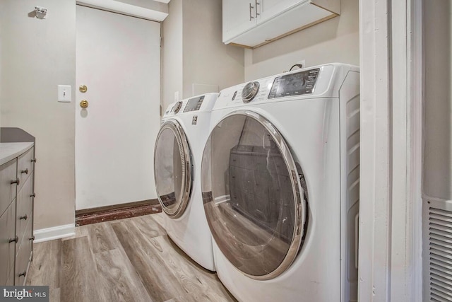 laundry area featuring washing machine and dryer, cabinet space, light wood-style flooring, and baseboards