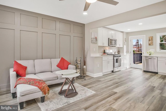 living area featuring baseboards, light wood finished floors, a ceiling fan, and recessed lighting