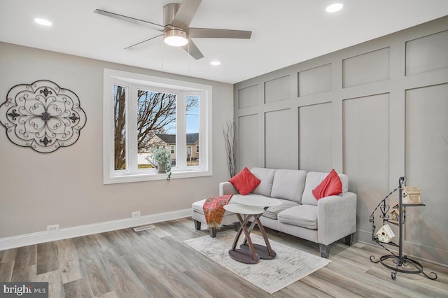 living area with a decorative wall, wood finished floors, a ceiling fan, and baseboards