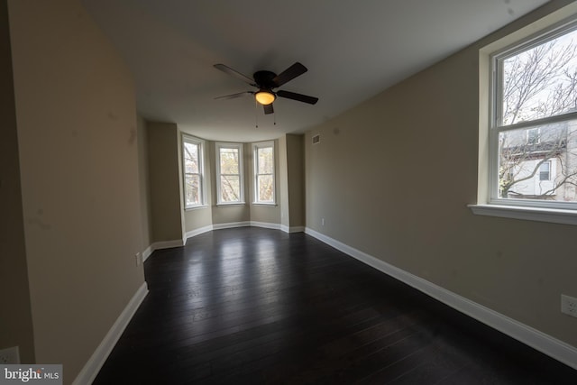 empty room featuring dark wood-style floors, visible vents, a ceiling fan, and baseboards