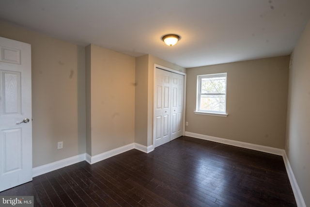 unfurnished bedroom featuring baseboards, dark wood finished floors, and a closet