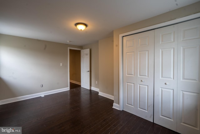 unfurnished bedroom with dark wood-style floors, baseboards, and a closet