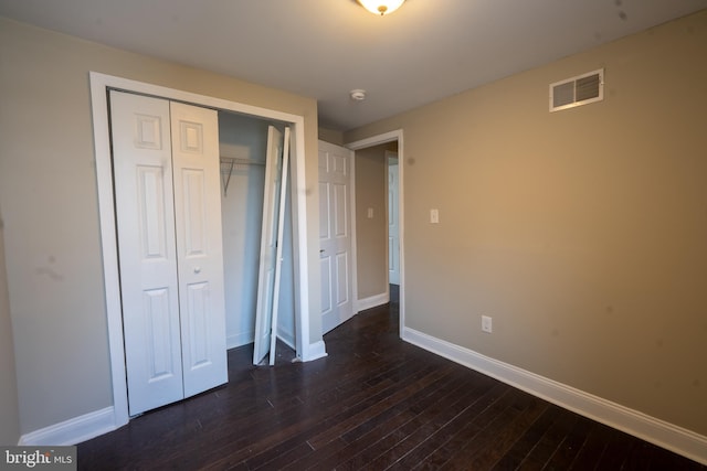 unfurnished bedroom featuring a closet, dark wood finished floors, visible vents, and baseboards