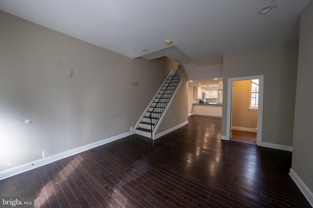 unfurnished living room featuring dark wood-type flooring, stairway, and baseboards