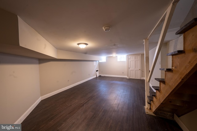 below grade area with dark wood-style floors, stairway, and baseboards