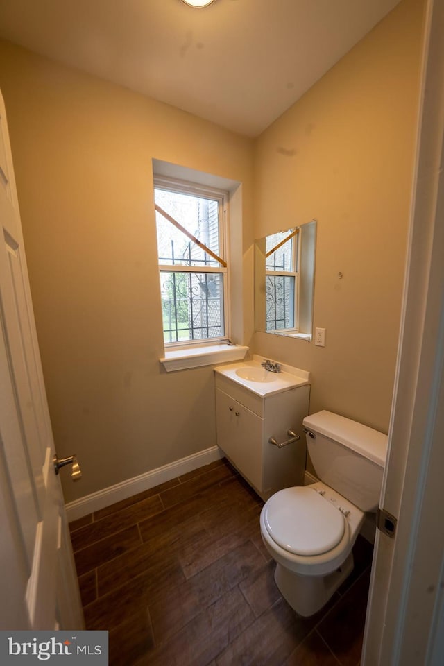 half bath featuring vanity, wood finished floors, toilet, and baseboards