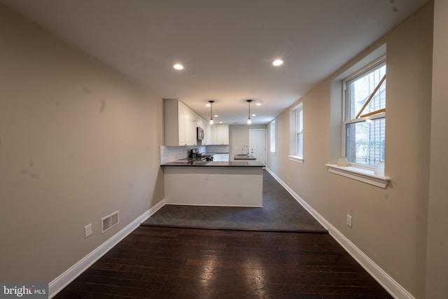 kitchen featuring visible vents, decorative backsplash, dark wood-type flooring, a peninsula, and baseboards