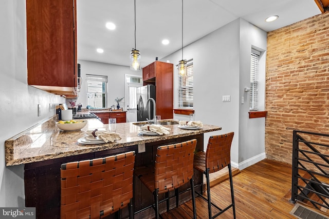 kitchen with a peninsula, decorative light fixtures, stainless steel refrigerator with ice dispenser, wood-type flooring, and a kitchen bar