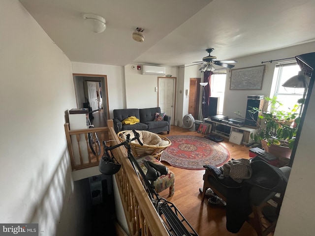 living area with a wall mounted AC, a ceiling fan, and wood finished floors