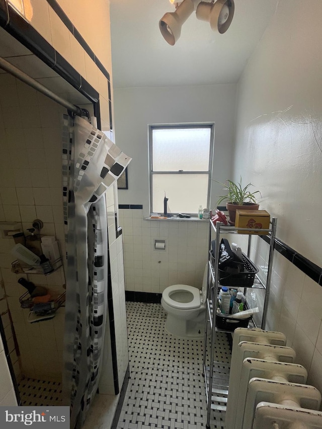 full bath featuring toilet, a stall shower, tile walls, wainscoting, and tile patterned flooring