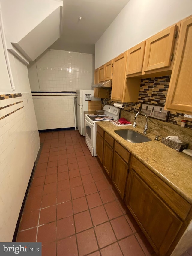 kitchen featuring dark tile patterned flooring, a sink, under cabinet range hood, backsplash, and white appliances