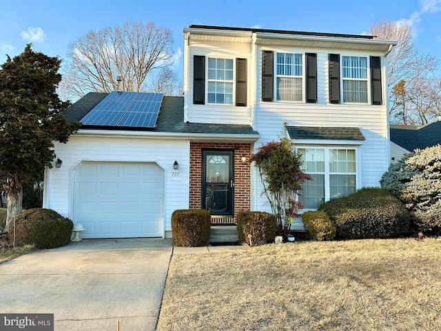 traditional-style house featuring driveway, roof with shingles, an attached garage, brick siding, and solar panels