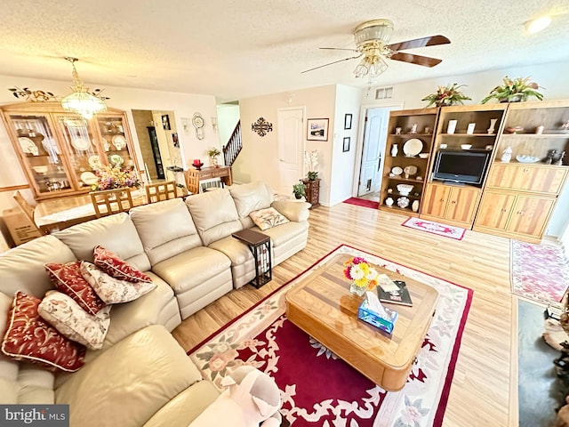 living area featuring wood finished floors, stairway, ceiling fan with notable chandelier, and a textured ceiling