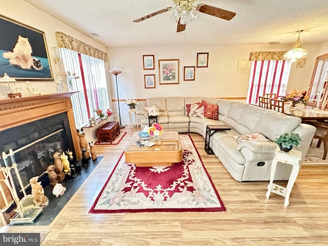 living area with a fireplace with flush hearth, a textured ceiling, wood finished floors, and a ceiling fan