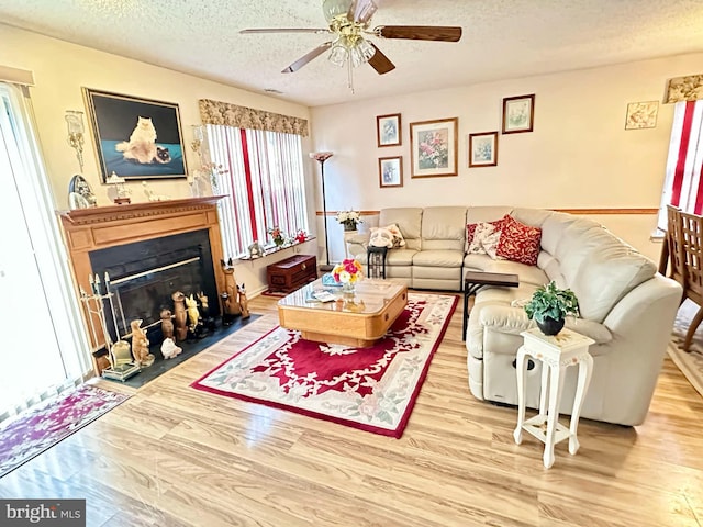 living area featuring a fireplace with flush hearth, a textured ceiling, ceiling fan, and wood finished floors